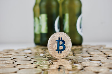 Cryptocurrency physical gold bitcoin coin on money near green beer bottles.