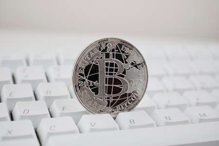 Digital currency physical silver bitcoin coin on white computer keyboard.の写真素材