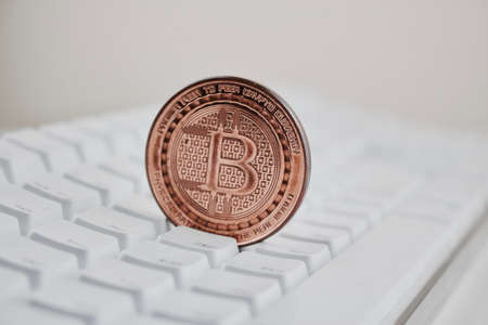 Digital currency physical brass bitcoin coin on white computer keyboard.の写真素材