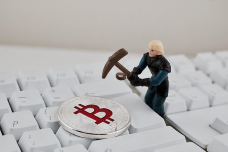Digital currency physical silver bitcoin coin on white keyboard near miner.