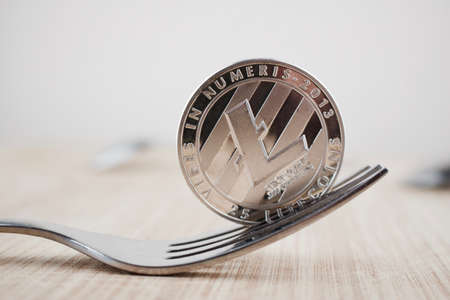 Digital currency physical silver Litecoin coin on silver fork. Wooden board.の写真素材