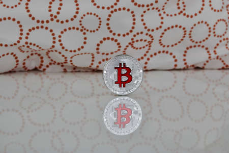 Cryptocurrency physical silver bitcoin coin with red sign on the white and orange scene.の写真素材