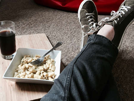 Tasty and fresh pasta in square plate on the floor near legs. Student lifestyle.の写真素材