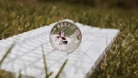 Europe leaving. Big silver brexit coin with british map on the white keyboard in grass.の写真素材