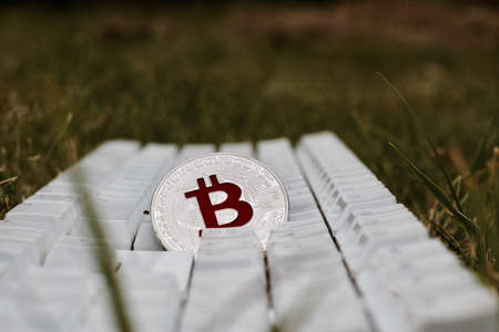 Digital currency physical silver bitcoin coin with red sign on white keyboard in green grass.の写真素材