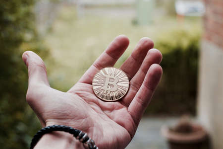 Digital currency physical gold bitcoin coin on man hand with bracelet.の写真素材
