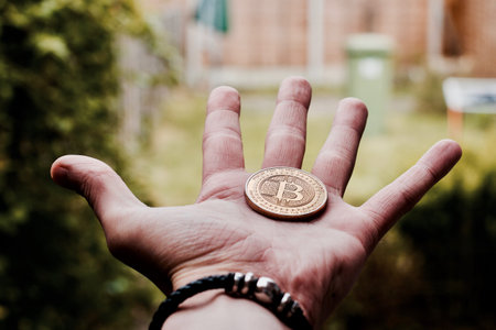 Digital currency physical gold bitcoin coin in man hand with black bracelet.の写真素材
