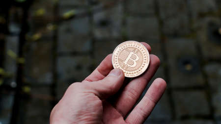 Digital currency physical gold bitcoin coin in man hand with black bracelet.の写真素材