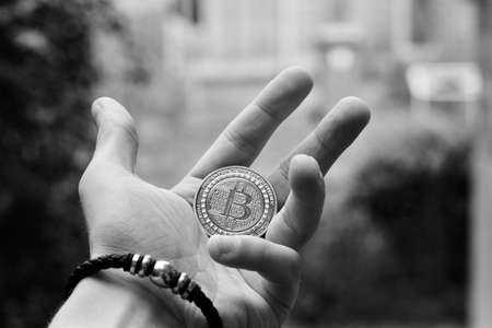 Digital currency physical gold bitcoin coin in man hand with black bracelet.の写真素材