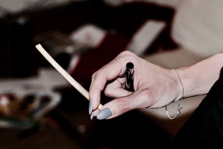 Woman hand with infinity bracelet black pencil and long marijuana joint.の写真素材