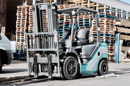 Big blue fork lift truck outdoor near wooden blue, red and natural pallets.