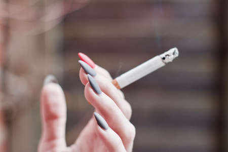 Young girl smoking cigarette and holding in hand with grey and pink nails on fingers.の写真素材