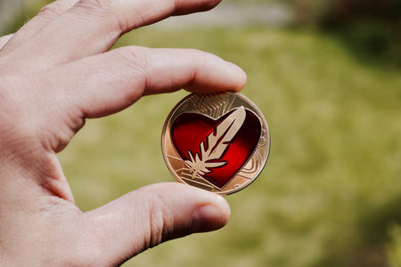 Gold coin with red big heart on man hand in green natural background. Love.
