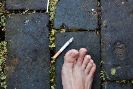 Naked white feet near cigarette on the stone floor outdoor. Danger.