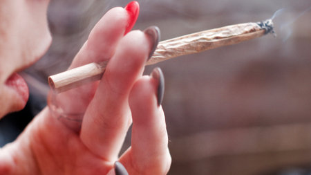 Young woman smoking marijuana spliff and holding in hand with pink and grey nails.