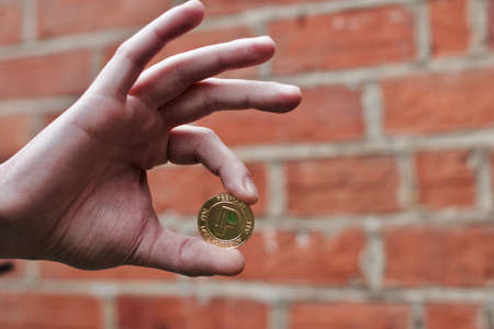 Digital currency physical gold peercoin coin in man hand near brick wall.の写真素材