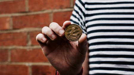 Digital currency physical gold litecoin coin in man hand near brick wall.の写真素材