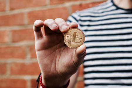 Digital currency physical gold litecoin coin in man hand near brick wall.の写真素材