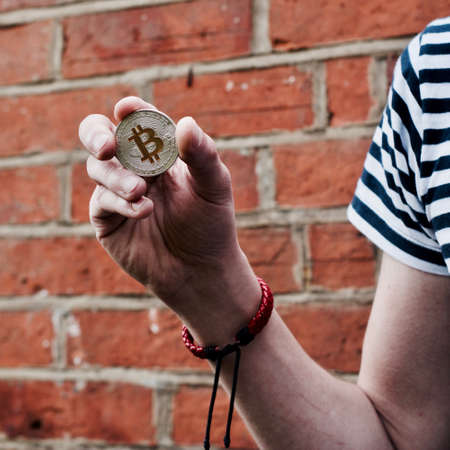 Digital currency physical metal bitcoin coin in hand. Man line tshirt. Brickwall.の写真素材