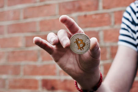 Digital currency physical metal bitcoin coin in hand. Man line tshirt. Brickwall.の写真素材