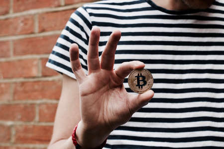 Digital currency physical metal bitcoin coin in hand. Man line tshirt. Brickwall.の写真素材