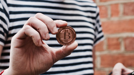 Digital currency physical metal bitcoin coin in hand. Man line tshirt. Brickwall.