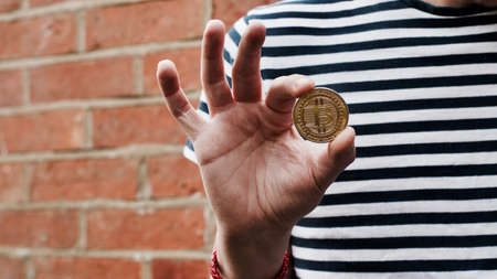 Digital currency physical metal bitcoin coin in hand. Man line tshirt. Brickwall.の写真素材