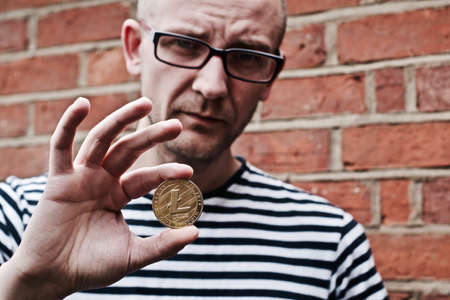 Young white man holding litecoin coin in his hand. Outdoor brickwall concept.の写真素材