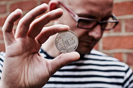 Young white man holding litecoin coin in his hand. Outdoor brickwall concept.の写真素材
