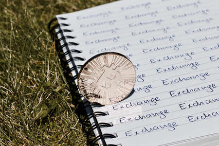 Digital currency physical metal bitcoin coin on the notebook with exchange inscription. Money outdoor concept.の写真素材