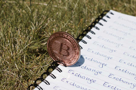 Digital currency physical metal bitcoin coin on the notebook with exchange inscription. Money outdoor concept.の写真素材