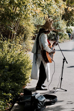 Man in white jacket on park playing on guitar. Natural music concept.