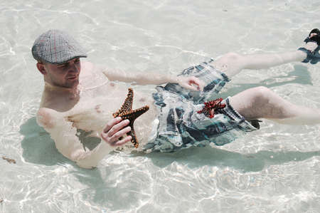 Young man in the water with a starfish in his hand.の写真素材