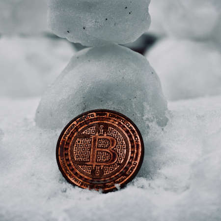 A physical digital currency metal coin on snow,  Cryptocurrency bitcoin conceptの写真素材