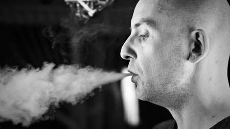 Bald young man smoking electronic cigarette. Vaping concept.の写真素材