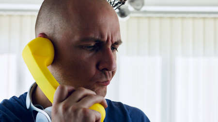 Young bald men talking to yellow phone. Communication concept.の写真素材