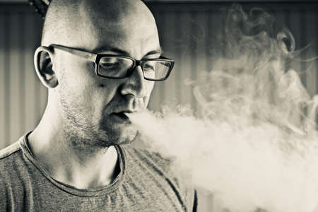 Young bald man smoking e-cigarette to quit tobacco. Vapor and alternative nicotine free smoking concept.の写真素材