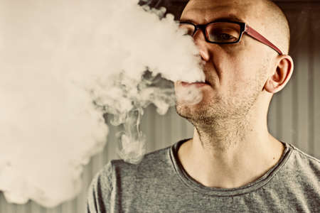 Young bald man smoking e-cigarette to quit tobacco. Vapor and alternative nicotine free smoking concept.の写真素材