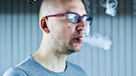 Young bald man smoking e-cigarette to quit tobacco. Vapor and alternative nicotine free smoking...