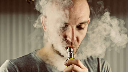 Young bald man smoking e-cigarette to quit tobacco. Vapor and alternative nicotine free smoking concept.の写真素材
