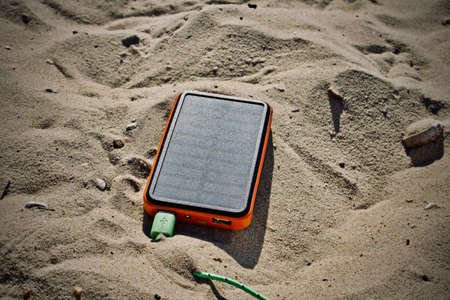 Orange solar energy charger on the beach. Usb socket with a green cable.の写真素材