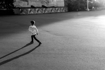 a little boy is walking on the road at sunset, casting a shadowの写真素材