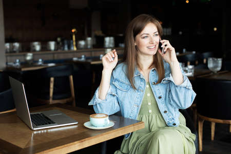 young girl drinking coffee and talking on the phoneの写真素材