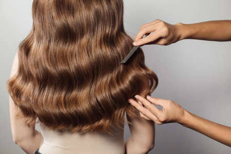 Closeup of female hands of hairdresser or coiffeur makes hairstyle. Hairの写真素材