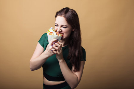 Close up of hungry girl with opened mouth, holding and eating big hamburger. Pretty woman with...