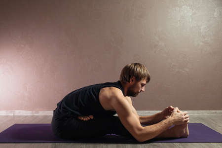 Young sporty man practicing yoga, meditating in Half Lotus pose, working out, wearing sportswear, indoor full length, brown yoga studioの写真素材