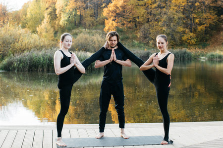 Young women and man doing yoga asana in the nature with the lake view. Evening workout outdoors, sports and healthy lifestyleの写真素材