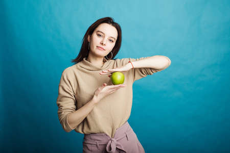 Image of a happy young girl standing on a blue background holding a green appleの写真素材