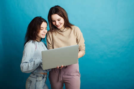 Image of happy young girls standing isolated over blue background and looking at laptopの写真素材