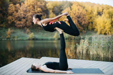 Young women and man doing yoga asana in the nature with the lake view. Evening workout outdoors, sports and healthy lifestyleの写真素材